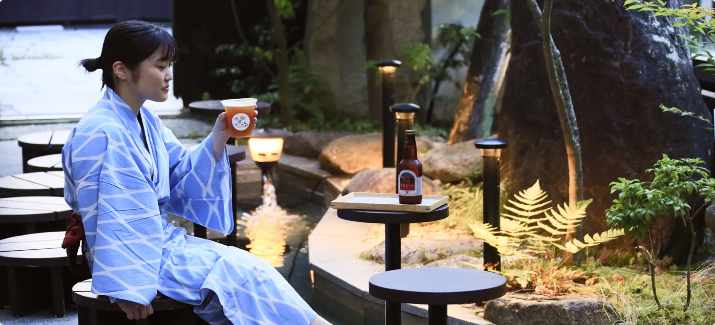 浴衣姿の女性が足湯に浸かりながら飲み物を楽しんでいる様子